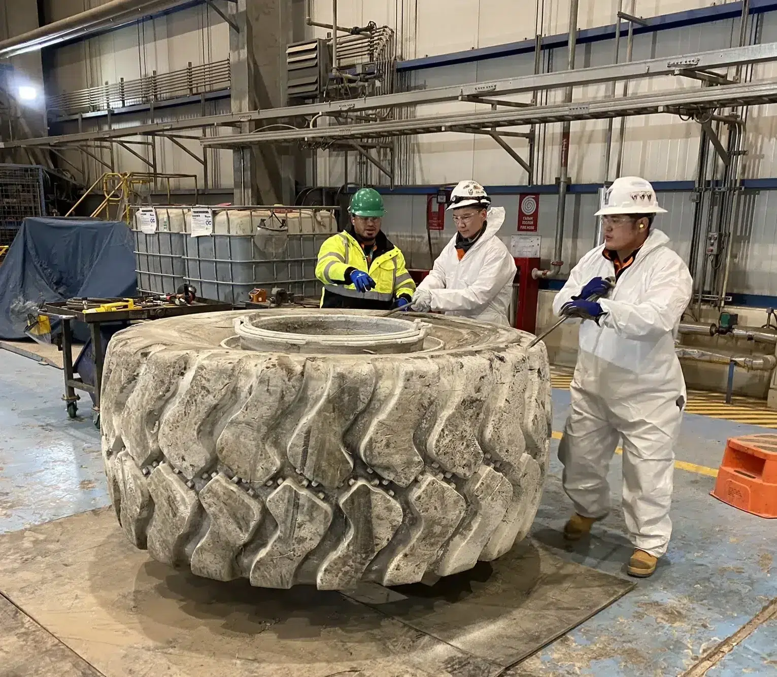 Three **otr** workers standing next to a large tire in a factory.