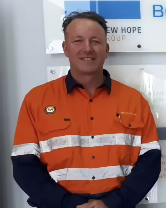 A man in an orange shirt standing in front of a sign off the road.