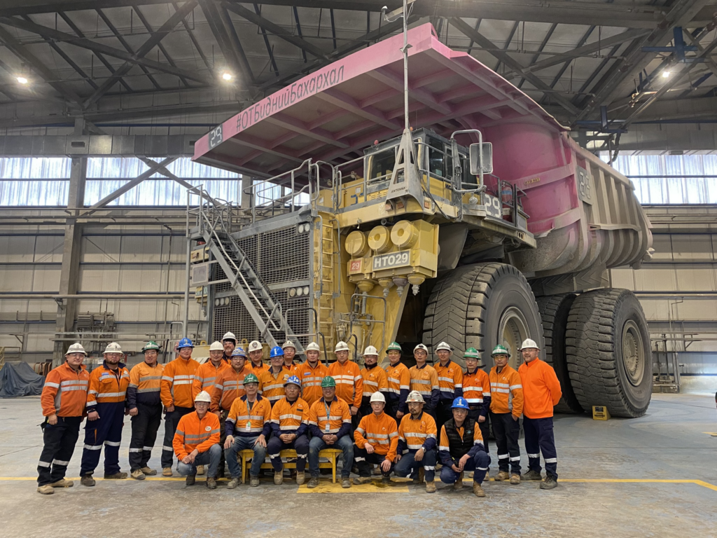 A group of people posing in front of an OTR pink dump truck by Klinge.