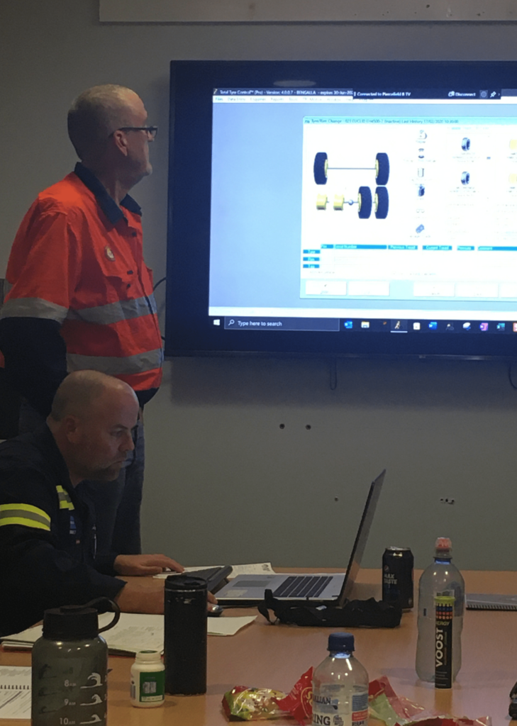 A group of people sitting at a table in front of a screen off the road.